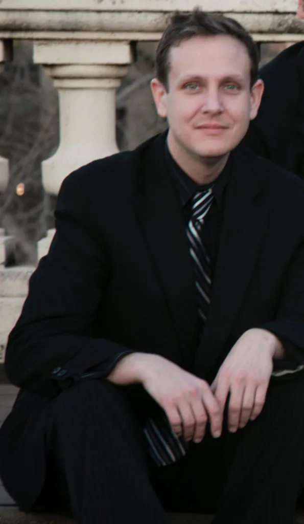 A man in black suit and tie sitting on the ground.